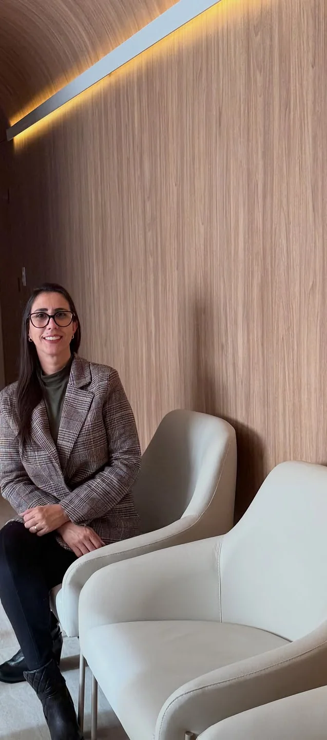 Débora sentada numa poltrona clara na sala de espera da Clínica Allmare