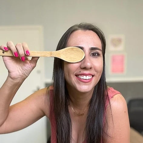 Débora sorrindo, segurando uma colher de pau na frente de um dos olhos