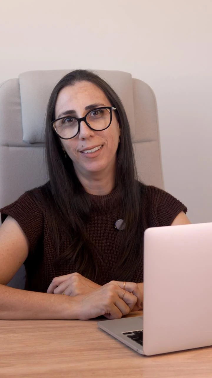 Débora Coelho no consultório, de óculos, com o notebook à frente
